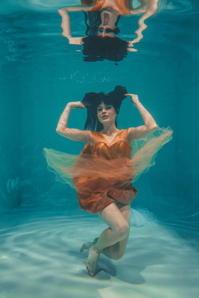 красива модель дівчина плаває під водою в помаранчевій сукні і насолоджується релаксацією і відсутністю стресу
 - Фото, зображення