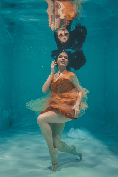 美しいモデルの女の子は、オレンジのドレスで水中を泳ぐありリラクゼーションとストレスの欠如 - 写真・画像