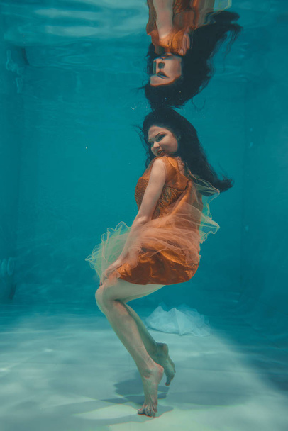 belle fille modèle nage sous l'eau en robe orange et jouit de détente et de manque de stress
 - Photo, image