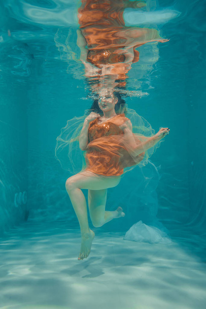 beautiful model girl swims underwater in orange dress and enjoys relaxation and lack of stress - Fotó, kép