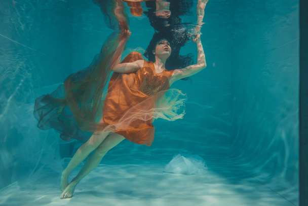 beautiful model girl swims underwater in orange dress and enjoys relaxation and lack of stress - Photo, Image
