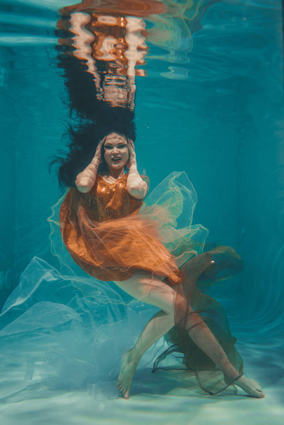 beautiful model girl swims underwater in orange dress and enjoys relaxation and lack of stress - Photo, Image