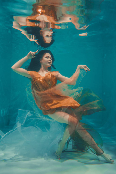 krásný model dívka plave pod vodou v oranžové šaty a má relaxační a absence stresu - Fotografie, Obrázek