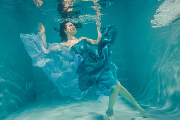 beautiful model girl swims underwater in blue dress and enjoys relaxation and lack of stress - Photo, Image
