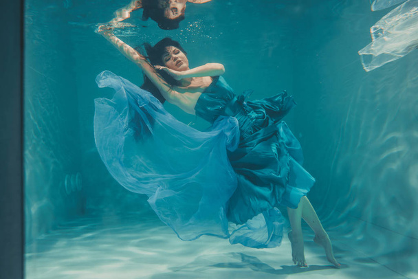 mooi model meisje onder water zwemt in blauwe jurk en geniet van de ontspanning en het ontbreken van stress - Foto, afbeelding