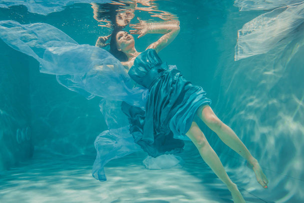 bela menina modelo com longos cabelos pretos nada debaixo d 'água em vestido azul à noite e gosta de relaxamento e falta de estresse
 - Foto, Imagem