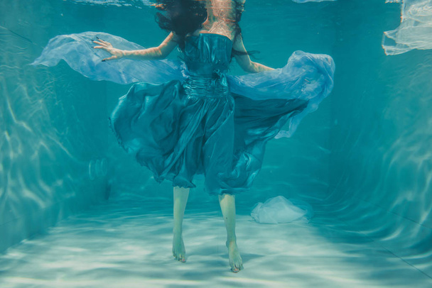 uzun siyah saçlı güzel model kız su altında mavi elbise ve rahatlama ve stres eksikliği sahiptir akşam yüzer - Fotoğraf, Görsel