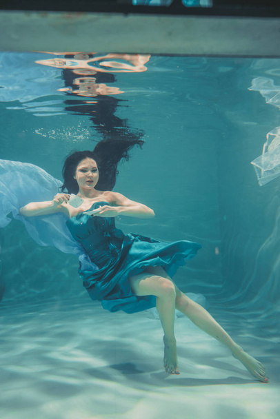 divertida chica divirtiéndose y beber té calmante para el desayuno, mientras que la natación meditativamente bajo el agua en un vestido
 - Foto, Imagen