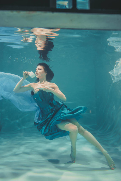 funny girl having fun and drinking soothing tea for Breakfast while meditatively swimming underwater in a dress - Photo, Image