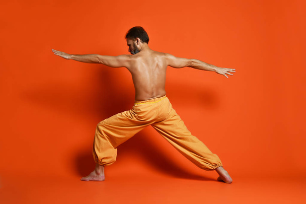 Old man practicing yoga doing stretching exercises against orange background - Φωτογραφία, εικόνα