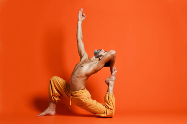 Viejo practicando yoga haciendo ejercicios de estiramiento sobre fondo naranja
 - Foto, imagen