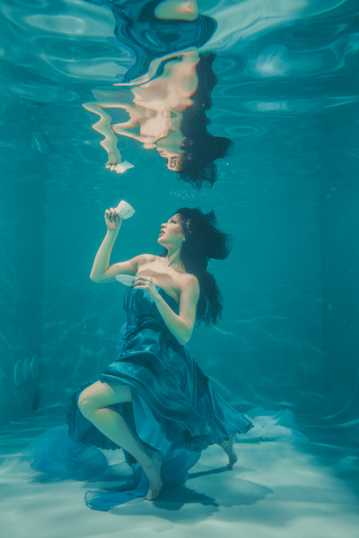 funny girl having fun and drinking soothing tea for Breakfast while meditatively swimming underwater in a dress - 写真・画像