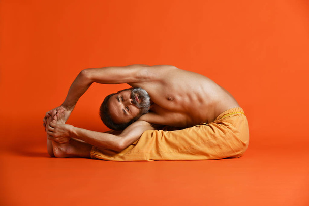old man practices Ashtanga Vinyasa yoga back bending asana Paschimottanasana - seated forward bend - 写真・画像