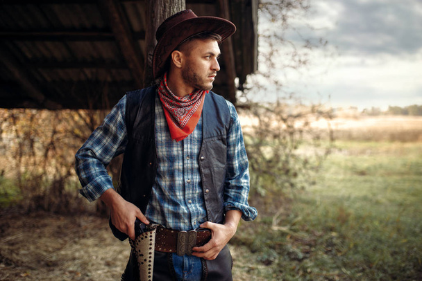 Βάναυση καουμπόη με το χέρι για το περίστροφο, Τέξας ranch στο παρασκήνιο, Δυτική. Εκλεκτής ποιότητας αρσενικό πρόσωπο με όπλο, άγρια Δύση lifestyle - Φωτογραφία, εικόνα