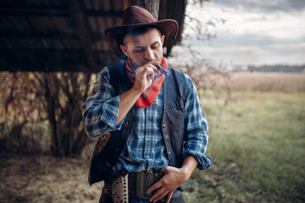 Brutális cowboy dohányzik, szivar, texas ranch-a háttér, a nyugati. Vintage férfi, akit fegyverrel a farm, vadnyugat - Fotó, kép