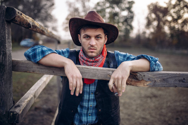 Брутальные ковбойские позы на лошадином загоне, ранчо в Техасе, вестерн. Винтажный мужчина на ферме, образ жизни дикого запада
 - Фото, изображение