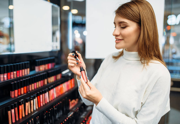 Female customer looks on lip liner in cosmetics store. Woman against showcase in beauty shop - Fotoğraf, Görsel