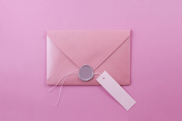 Pink envelope-letter with a wax seal and a paper tag for a signature on a light purple background. - Foto, imagen