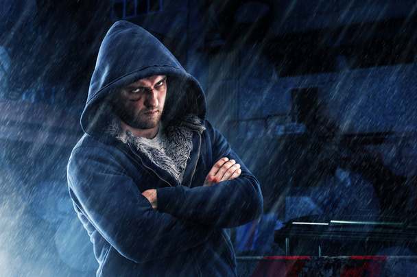 Ύποπτος άνδρας με μελανιά και γροθιές νοκ σε hoodie δρόμο το βράδυ στη βροχή. Ποινικά πρόσωπο, χούλιγκαν μαχητής - Φωτογραφία, εικόνα