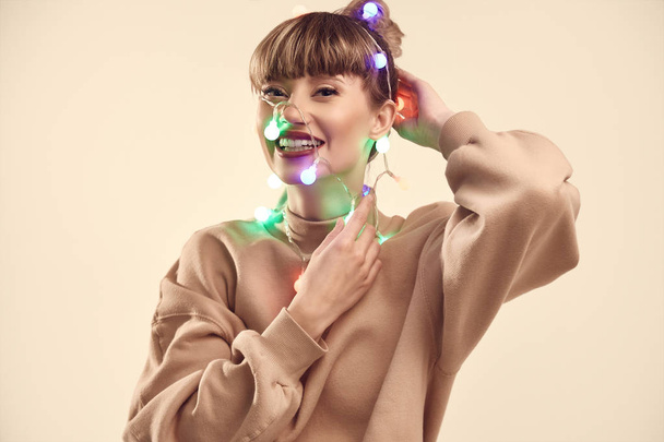 Retrato positivo brillante de la manera de la mujer rubia hermosa con las luces de Navidad en la cabeza. Sesión de estudio
. - Foto, Imagen