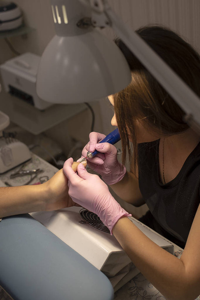 In the nail salon client manicurist in pink gloves removes varnish with manicure device - Photo, Image