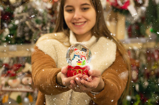 Sıcak palto Noel Fuarı'nda bir alışveriş merkezinde firtrees, ev ve yapay kar ile cam topa tutan kız. Kış ruh hali - Fotoğraf, Görsel