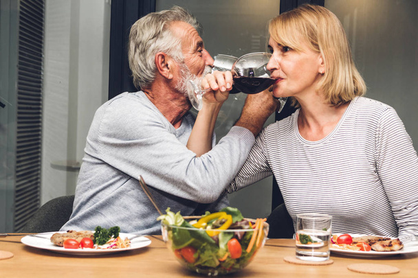 Senior couple relax eating dinner and drinking wine glasses together in the kitchen at home.Retirement couple concept - Photo, Image
