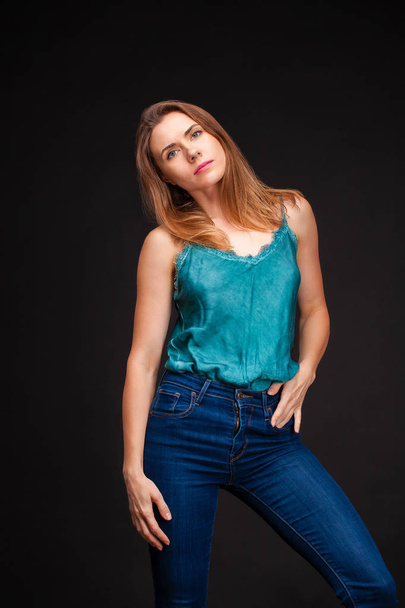 Fashion shoot of young sexy woman in blue jeans and green blouse in dark studio - Fotoğraf, Görsel