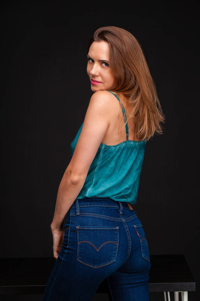 Fashion shoot of young sexy woman in blue jeans and green blouse in dark studio - Foto, afbeelding