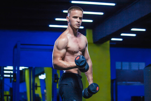 Powerful man doing exercises with dumbbells. Photo of sporty muscular male in the gym. Strength and motivation - Foto, Imagen