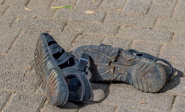 Пара сломанных и заброшенных старых сандалий, изолированных снаружи на тротуаре изображения с копией пространства в ландшафтном формате
 - Фото, изображение