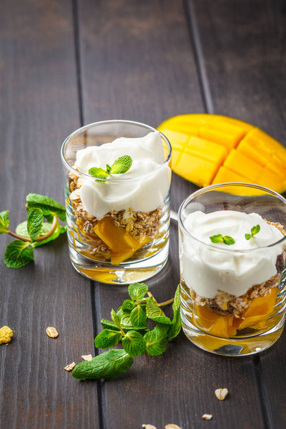 Greek yogurt mango granola parfait in a glass on a dark wooden background. - Фото, зображення