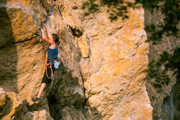 Tyttö kiipeää kalliolle. Kiipeilijä harjoittelee kiipeämistä. Vahva urheilija voittaa vaikean kiipeilyreitin. Äärimmäinen harrastus. Nainen harrastaa urheilua luonnossa. Luonnon kivinen maasto
. - Valokuva, kuva