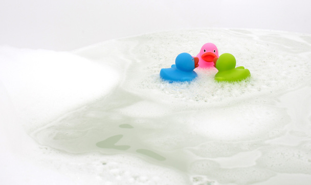 Roze, groene en blauwe eend in een badkuip, omgeven door zeep - Foto, afbeelding
