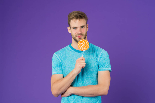 Taste of childhood. Man handsome macho eat big colorful sweet lollipop. Man with bristle likes lollipop. Cheat meal concept. Sugar harmful for health. Guy hold lollipop candy violet background - Photo, Image