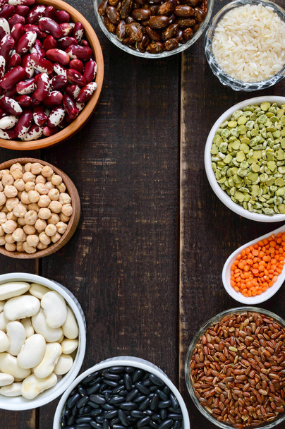 Healthy food, dieting, nutrition concept, vegan protein and carbohydrate source. Assortment of colorful raw legumes: red lentils, green peas, beans, chickpeas ; brown and white rice in bowls on a wooden table. Top view, flat lay background - Photo, Image