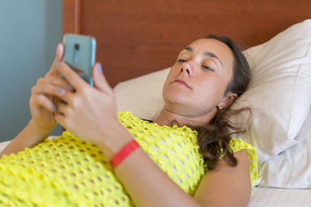 Fiatal nő a smartphone-a reggel, az ágyban fekve. Nő az ágyban, szociális apps, smartphone ellenőrzése. - Fotó, kép