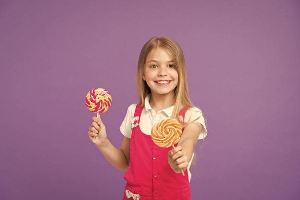 Food and dessert. Girl smile with lollipops on violet background. Happy kid with swirl caramels on purple background. Small child smiling with candies on sticks. Deliciously sweet. Diet and dieting - Foto, afbeelding