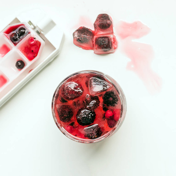 Cocktail aus in Eiswürfeln gefrorenen Beeren (Himbeeren, Brombeeren, rote und schwarze Johannisbeeren). sommerliches Erfrischungsgetränk. Selektiver Fokus. - Foto, Bild