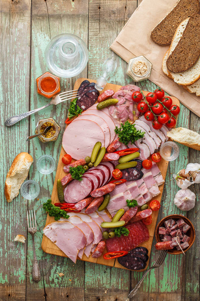 Assorted sausages and smoked meat with pickles, bread and vodka on wooden board, top view copy space - Fotoğraf, Görsel