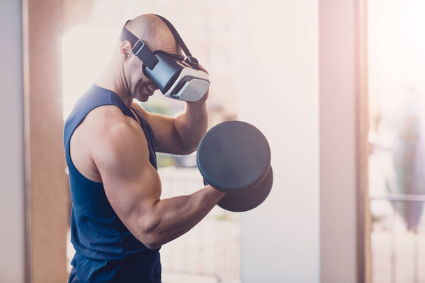 Man wearing virtual reality glasses with dumbbells - 写真・画像
