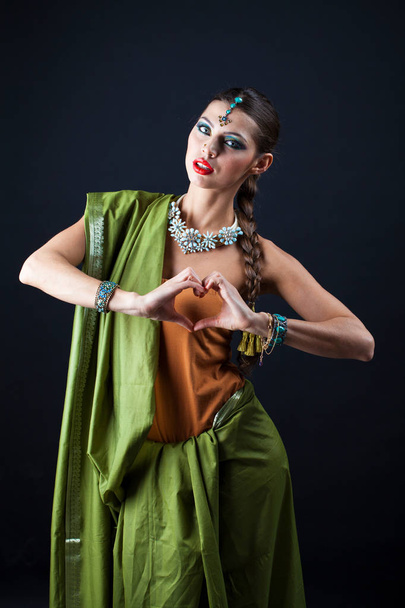 Fashion portrait of pretty sexy young brunette woman in green sari posing on dark studio background  - 写真・画像