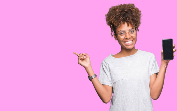 Молодая африканская американка показывает смартфон на изолированном фоне очень счастливо указывая рукой и пальцем в сторону
 - Фото, изображение