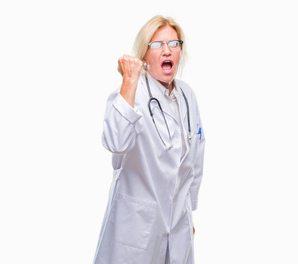 Middle age blonde doctor woman over isolated background angry and mad raising fist frustrated and furious while shouting with anger. Rage and aggressive concept. - Foto, immagini