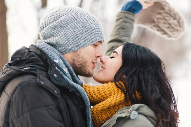 Happy woman and man, kissing, and huging, spending time together enjowing eachother, snow, life, winter. Portrait wonderful young couple wearing stylish wool hats and scarfs. - Foto, imagen