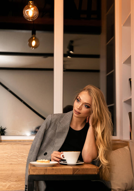Beautiful young blonde woman with a cup of coffee in a cafe - Фото, зображення