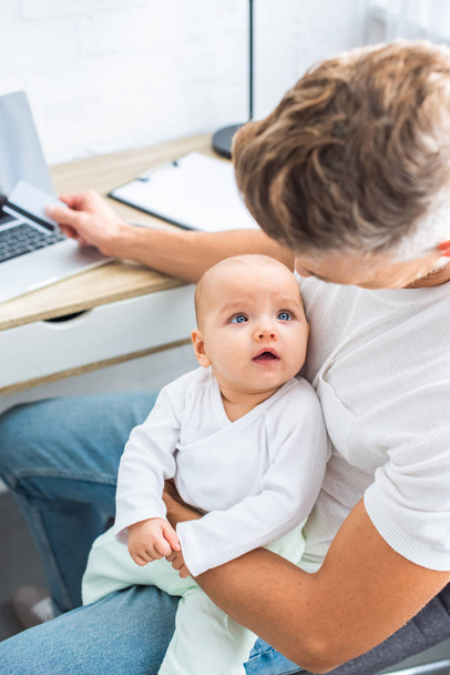 padre sentado en el escritorio de la computadora con tarjeta de crédito y mirando a la hija bebé
  - Foto, imagen
