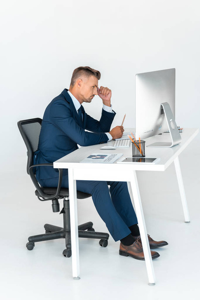 side view of serious handsome businessman looking at computer isolated on white - Fotografie, Obrázek