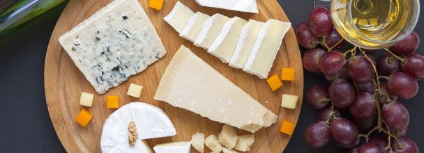Tasting cheese with wine, fruits, pretzels and walnuts, from above.Top view. Flat lay. Dark surface. - Photo, Image