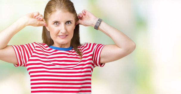 Взрослая женщина средних лет носит повседневную футболку на изолированном фоне, улыбаясь, дергая за уши пальцами, смешной жест. Задача прослушивания
 - Фото, изображение